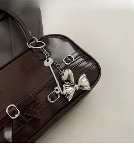 Détail du sac à main brillant marron foncé avec breloques argentées et nœud papillon