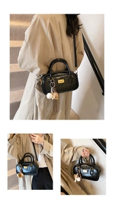 Black patent Boston handbag detail view, featuring gold metal tag and cute baseball pendant charms.