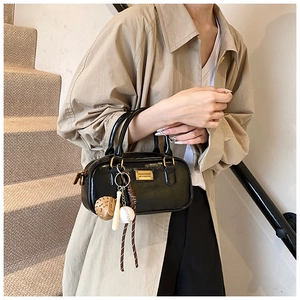 Detailed view of black patent leather Boston bag with charm and metal tag on model.