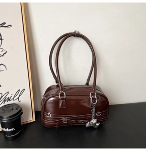 Détail du sac bandoulière marron foncé brillant avec nœud et pendentif cœur argenté