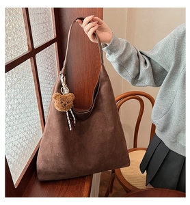 Detail of dark brown suede hobo bag with plush bear charm and patterned silk scarf decor