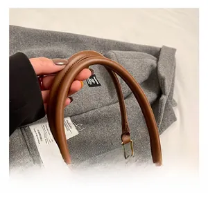 Détail des poignées en cuir marron et ferrures dorées sur un sac à carreaux