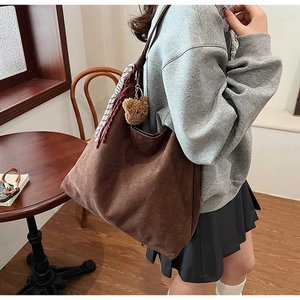 Brown suede tote bag with plush bear charm and striped scarf in a cozy cafe setting