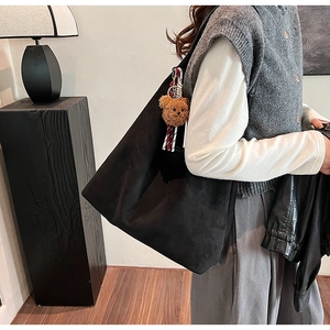 Macro detail of large black suede tote bag with cute plush bear charm on handle