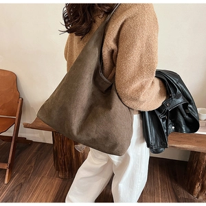 Detail view of a large brown suede hobo bag styled with a leather jacket in a room