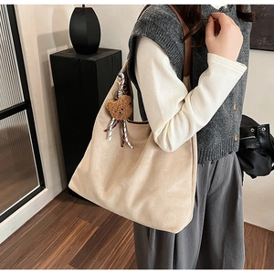 Detail view of large beige suede tote bag with brown leather strap and bear charm