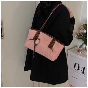 Pink suede tote bag with brown leather handles and a plush charm shown on shoulder