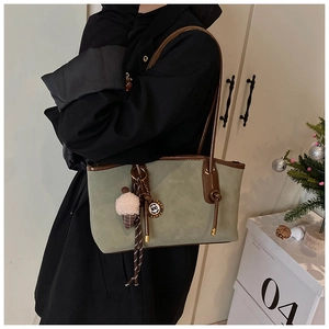 Detail of dark green tote bag with plush charm and brown leather straps on model