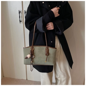 Detail of green suede tote bag with brown leather handles and brand charm decoration
