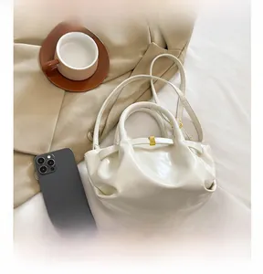 Close-up of cream glossy handbag with metal details on white linen background