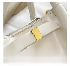 Macro detail of glossy gold buckle on white pleated leather bucket bag with fine stitching
