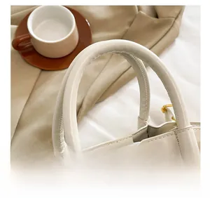 Detail of a beige leather handbag showing the cylindrical handle and neat stitching