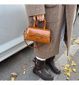 Close-up of brown vintage leather handbag with circular metal lock in autumn street setting