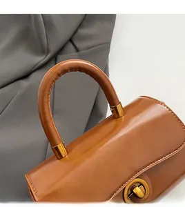 Detail of a brown leather handbag featuring a cylindrical handle and gold metal rotary lock