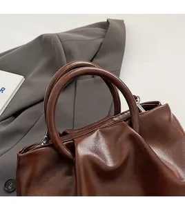 Vue macro d'un sac seau marron foncé avec cuir plissé souple et poignée cylindrique