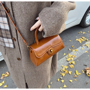 Detail of vintage caramel leather handbag featuring a golden round swivel lock and handle