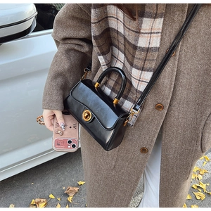Detail of a matte black leather handbag with a gold twist lock and a crossbody strap