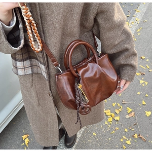 Détail d'un sac à main plissé marron foncé avec breloque et texture en cuir PU souple