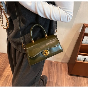 Detail of a dark olive green glossy leather handbag with gold metal twist-lock and top handle