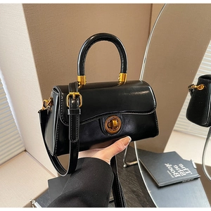 Detail of black handbag with gold rotary lock and adjustable shoulder strap