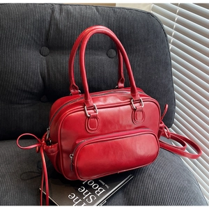 Detail of red Boston handbag with front zipper pocket and side bow on velvet