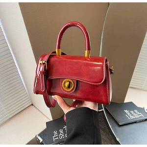 Detail of vintage red leather handbag featuring gold circular twist lock and smooth texture