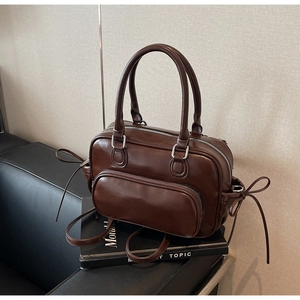 Detalle de bolso vintage de cuero marrón con cordones laterales y bolsillo frontal con cremallera