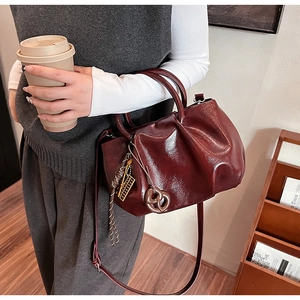 Détail du sac à main en cuir verni bordeaux avec plis et pendentif tressé élégant