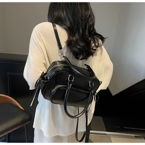 Detail of black faux leather backpack showing silver metal zippers and multi-pocket design