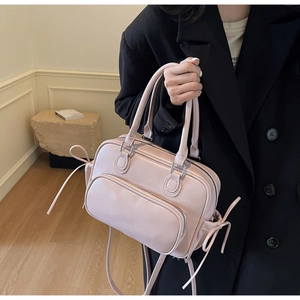 Detail of pink Boston bag featuring side ribbon bows and dual zipper compartments