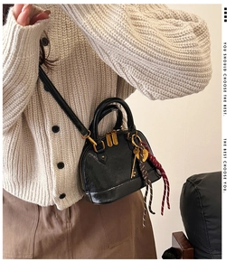 Detail of a black glossy leather mini shell bag featuring golden hardware and woven keychain