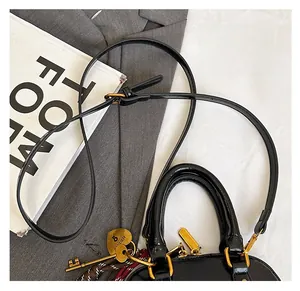 Detailed view of a black glossy leather handbag with heart lock charm on a grey suit