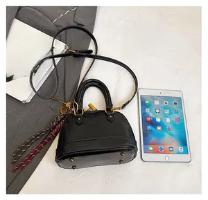 Top view of black shell handbag next to a tablet showing compact size and tassel detail