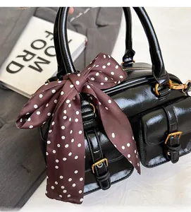 Detail of black glossy bowling bag featuring two buckled pockets and a silk polka dot bow