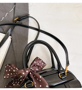 Detail of black glossy leather bowling bag with gold hardware and polka dot silk ribbon