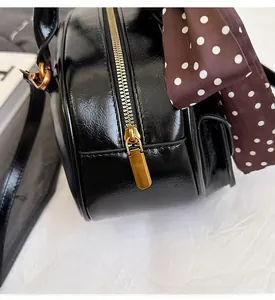 Detail of smooth gold zipper and black glossy bowling bag with a polka dot scarf accessory