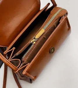 Detail view of smooth golden zipper and magnetic closure on brown leather crossbody bag