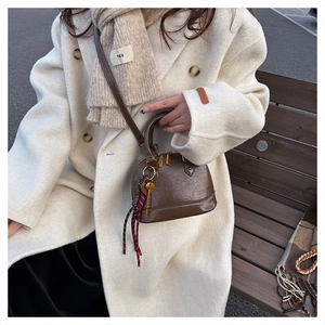 Detail of dark brown shell bag in oil wax leather with decorative scarf and key charm