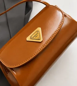 Close-up of vintage brown leather bag featuring a polished triangular metal logo detail