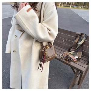 Detail of dark brown leather shell bag with gold zipper and leather tassel on a wool coat