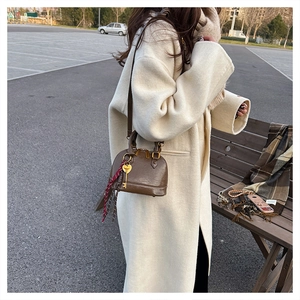 Close-up of brown textured shell bag with gold hardware and silk scarf on beige coat