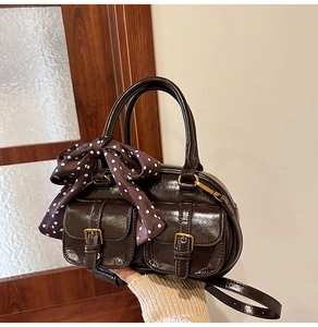 Detail of a dark brown glossy leather Boston bag with polka dot scarf and gold buckles