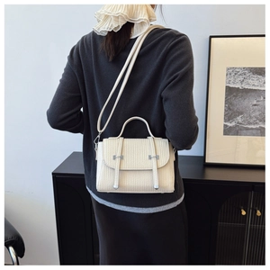 Close-up of beige textured small square bag with vertical embossing and metal buckles