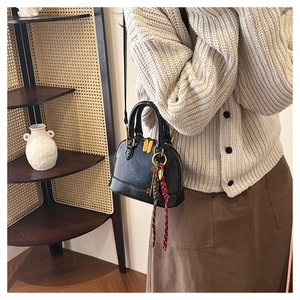 Detail of a black leather shell crossbody bag with braided pendant on a neutral background