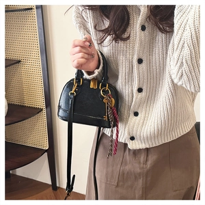 Detail of a black leather shell handbag with gold hardware and a tassel keychain