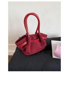 Close-up of burgundy suede handbag featuring bright red leather handle and textured finish