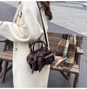 Detail of dark brown Boston bag with a vintage polka dot scarf on a wooden bench