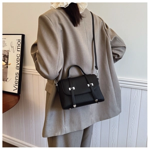 Detail of black pleated crossbody bag featuring silver buckle and stylish vertical stripes