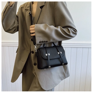 Detail view of a black vertical textured leather crossbody bag styled with a khaki blazer