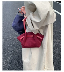 Close-up of a burgundy suede pleated handbag held by a model in a beige trench coat